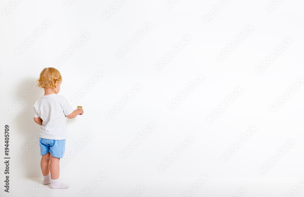 Little boy with paint brush standing back near white wall