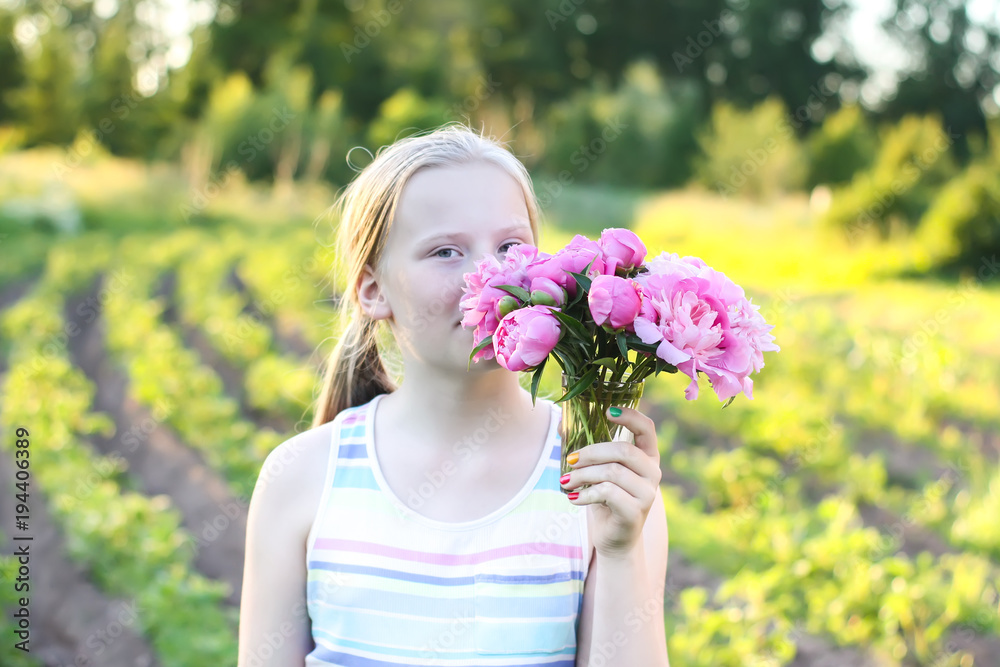 Little blond girl holding pink fresh peony flowers.