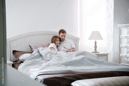 Couple lying and reading book in modern bedroom
