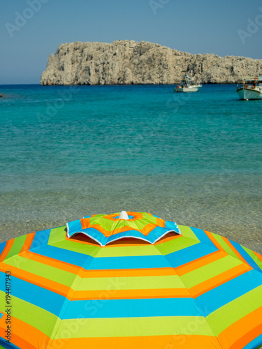 Astypalaia,Greece-August 2016.A colorful umbrella with the crystal clear waters in the background photo