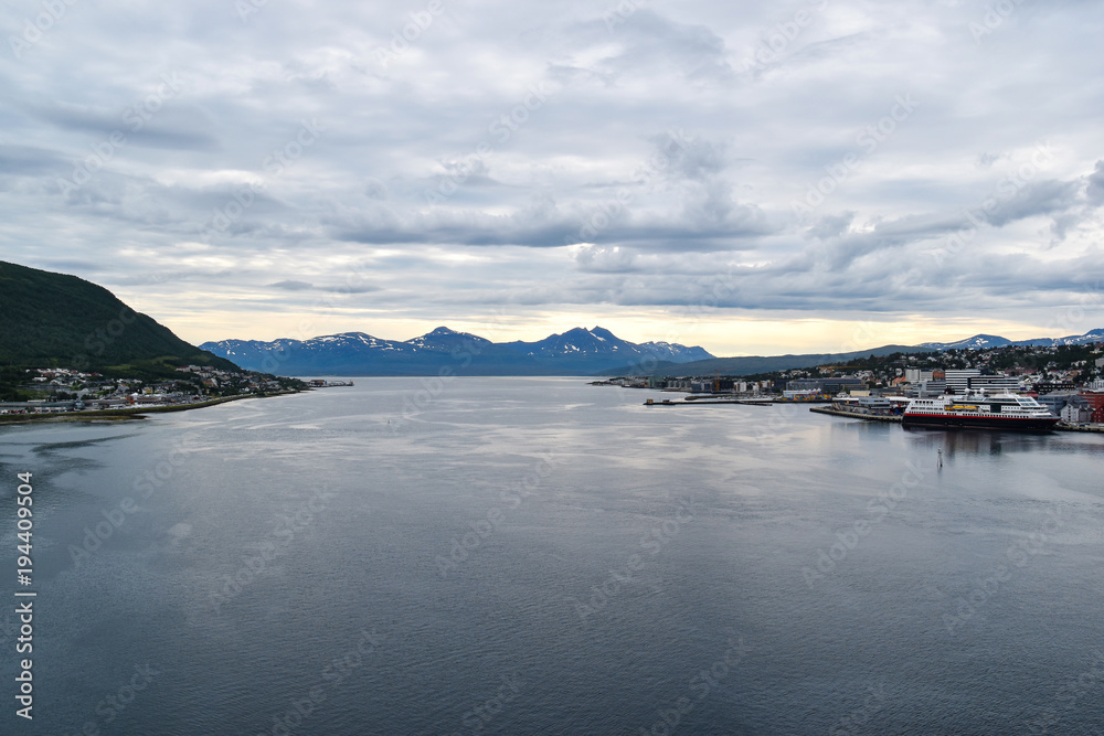 panoramic view of waterfront of Tromso, Norway with mountain range in background under overcast sky