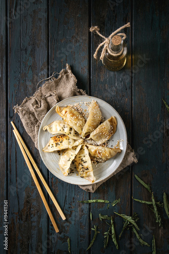 Asian dumplings Gyozas potstickers fried on ceramic plate, served with chopsticks and bottle of sauce over dark wooden plank background. Top view, space. Dark rustic style