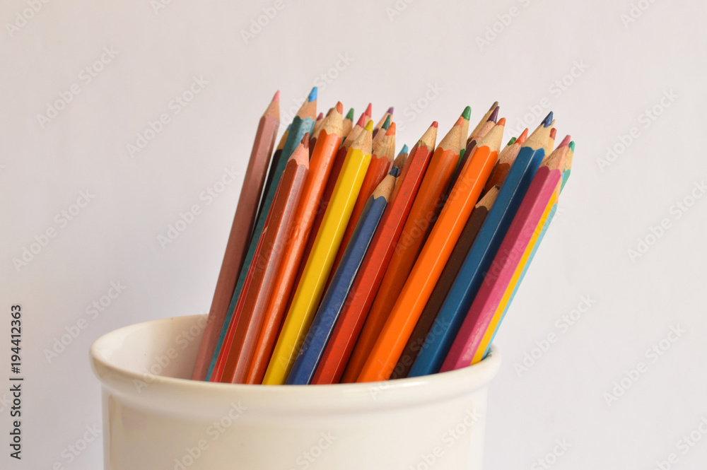 Colored pencils in jar on a pale background Colored pencils in jar on a pale background