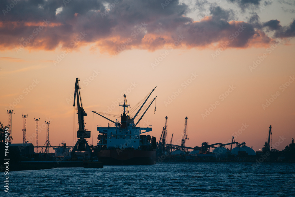 Silhouette on cargo ships and cranes in industrial harbor in sunset
