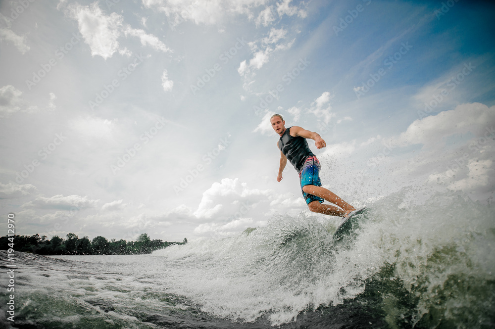 Athletic man wakesurfing on the board down the river against the sky