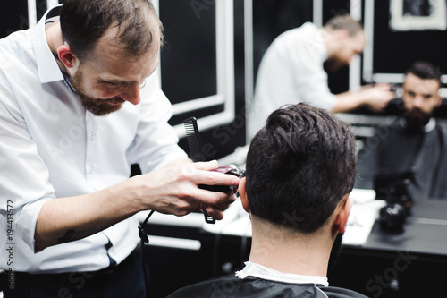 Master cuts hair and beard of men in the barbershop, hairdresser makes hairstyle for a young man