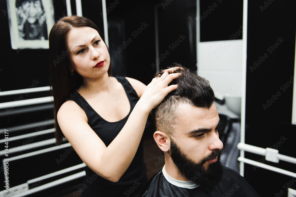 Fototapeta premium Master cuts hair and beard of men in the barbershop, hairdresser makes hairstyle for a young man