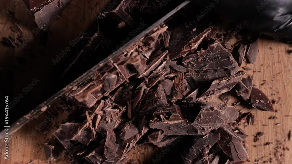 Chopping chocolate on cutting board on wooden table as baking ingredient preparation (slow motion) Chopping chocolate on cutting board on wooden table as baking ingredient preparation (slow motion)