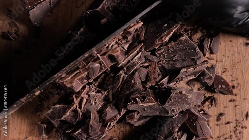 Chopping chocolate on cutting board on wooden table as baking ingredient preparation (slow motion) photo