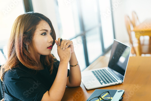 Asian stylish woman designer wear black dress and red lips working with her laptop and computer design appliances in coffee shop in selective focus..