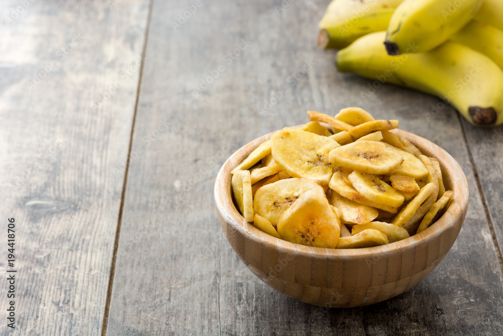 Banana chips in wooden bowl on wooden table background