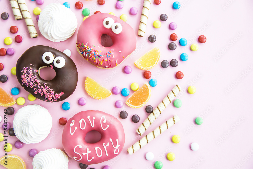 Junk food. Donuts, marmalade, chocolate sticks and balls, and meringues are scattered on a pink background. Unhealthy food concept. Top view, flat lay