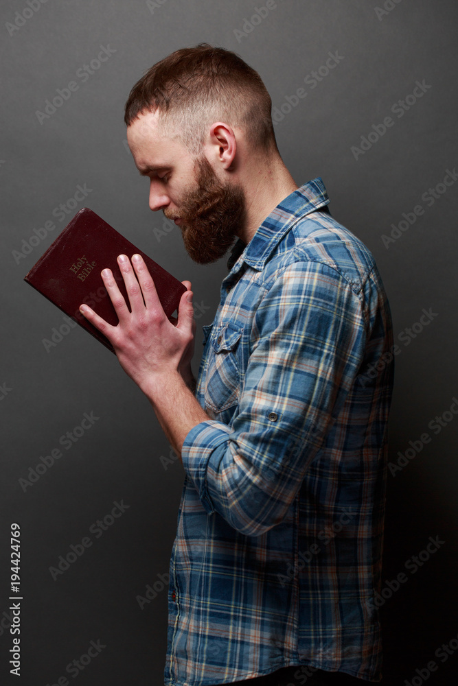 Handsone man reading and praying over Bible in a dark room over gray texture Handsone man reading and praying over Bible in a dark room over gray texture
