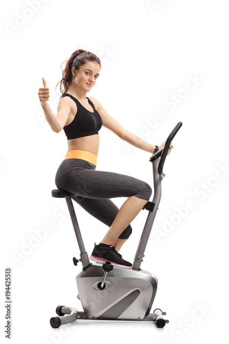 Fitness woman riding an exercise bike and making a thumb up sign