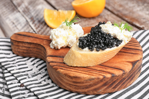 Sandwich with delicious black caviar and cottage cheese on wooden board