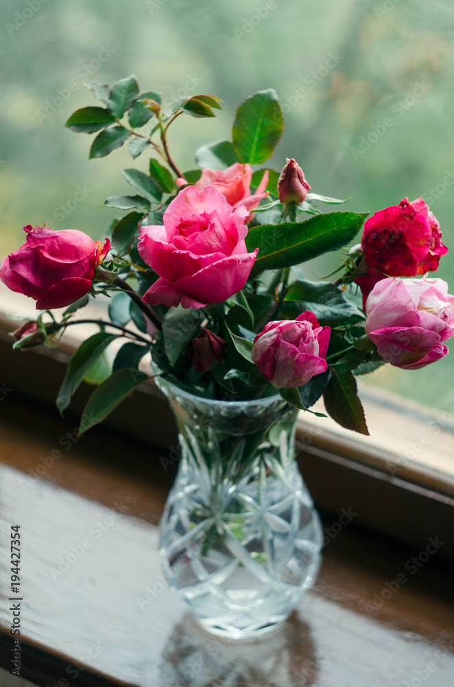 Homemade roses. Bouquet in a crystal vase on a wooden window. The concept of quiet and cozy village life, gardening and environmental friendliness Homemade roses. Bouquet in a crystal vase on a wooden window. The concept of quiet and cozy village life, gardening and environmental friendliness