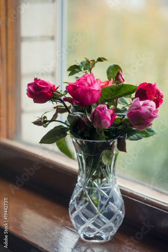 Homemade roses. Bouquet in a crystal vase on a wooden window. The concept of quiet and cozy village life, gardening and environmental friendliness