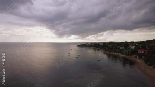 Aerial shot of resort on the coast. Shoreline and sea with boats, grey clouds in the sky. Trikorfo Beach, Greece photo