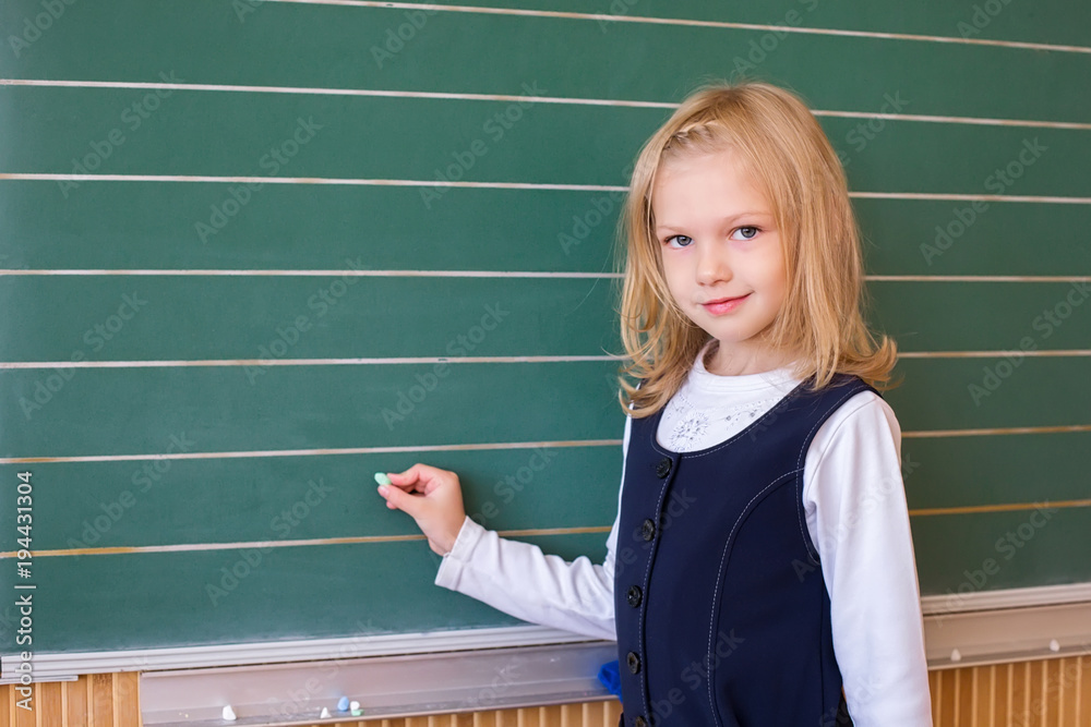 First grade pupil a girl writing on green blackboard at school lesson First grade pupil a girl writing on green blackboard at school lesson