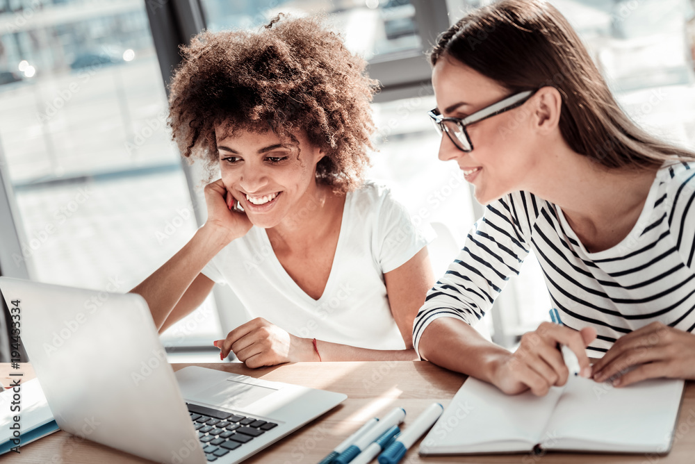 Interesting idea. Joyful positive nice women sitting together at the table and looking at the laptop screen while looking for interesting ideas Interesting idea. Joyful positive nice women sitting together at the table and looking at the laptop screen while looking for interesting ideas