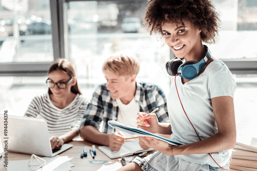 Fototapeta premium Working plan. Joyful positive attractive woman sitting on the table and wearing headphones while writing a working plan
