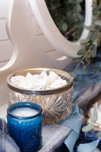 Wedding decor on a white boudoir table of a bride from a vase with sweets, tulle and a blue candle. Side view, selective focus