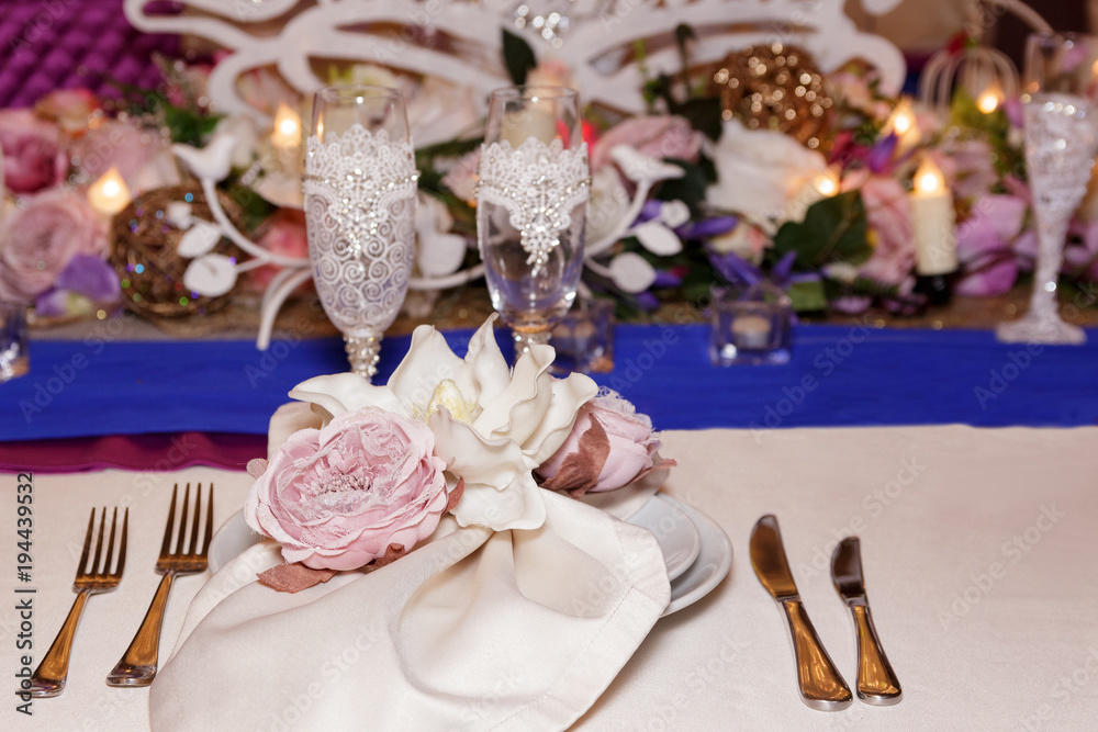 A wedding decor of white dishes, white bouquets with flowers, candles and glasses stand on a light tablecloth of a served table in a restaurant. Side view, selective focus A wedding decor of white dishes, white bouquets with flowers, candles and glasses stand on a light tablecloth of a served table in a restaurant. Side view, selective focus