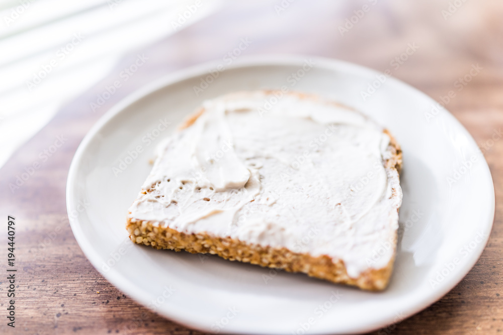 Closeup of slice piece of whole wheat sprouted toasted grain bread on plate with white cream cheese spread on table macro Closeup of slice piece of whole wheat sprouted toasted grain bread on plate with white cream cheese spread on table macro