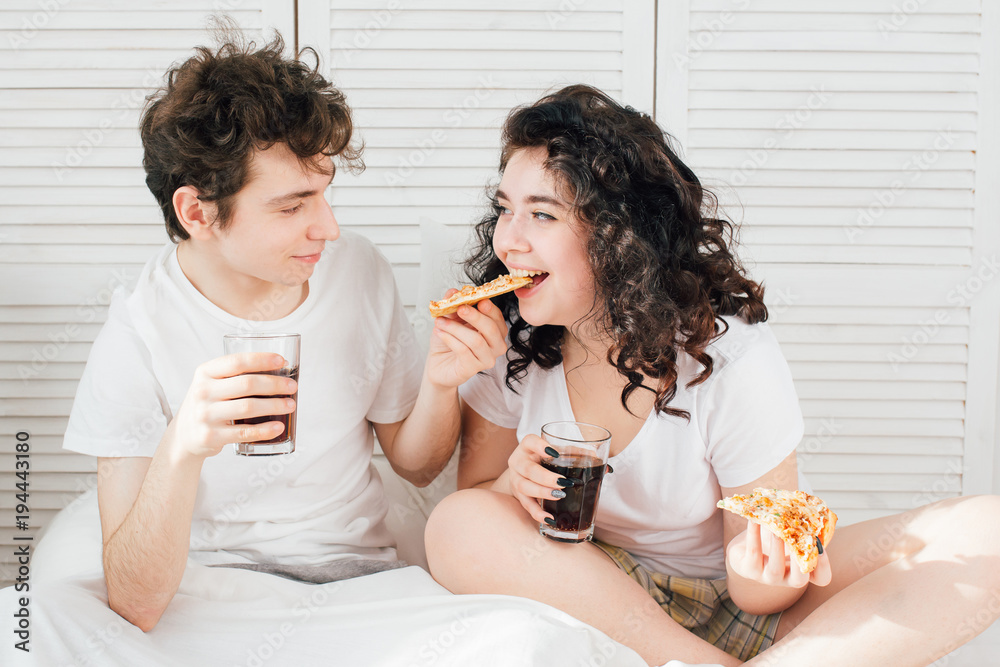 Couple watching TV in bed and eating pizza Couple watching TV in bed and eating pizza