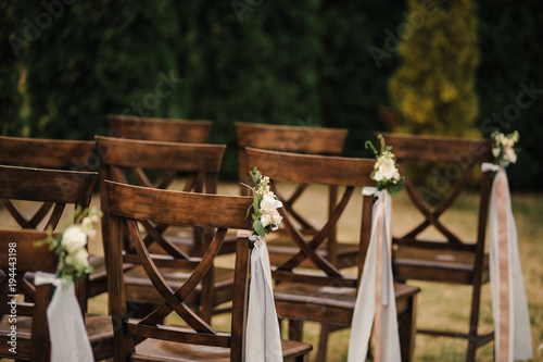 Very beautiful outside ceremony. classical wedding in forest. The arch is wooden. White flowers. Brown chairs. Rite. Bride and groom. Decor. Floristics. In the open air. Path from the petals of roses.