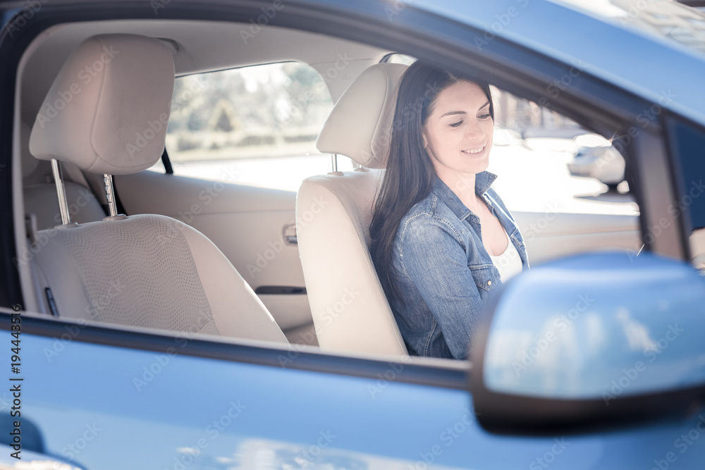 Be attentive. Pleasant pretty joyful woman smiling and looking down sitting in the car.