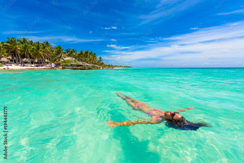 Fototapeta premium Atrakcyjna młoda kobieta relaksuje w turkusowych wodach morze karaibskie przed raj plażą w Tulum, blisko Cancun, Riviera Maya, Meksyk