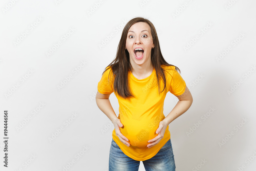 European young happy woman football fan or player with soccer ball under yellow uniform as pregnant with big belly isolated on white background. Sport play football, health, healthy lifestyle concept. European young happy woman football fan or player with soccer ball under yellow uniform as pregnant with big belly isolated on white background. Sport play football, health, healthy lifestyle concept.