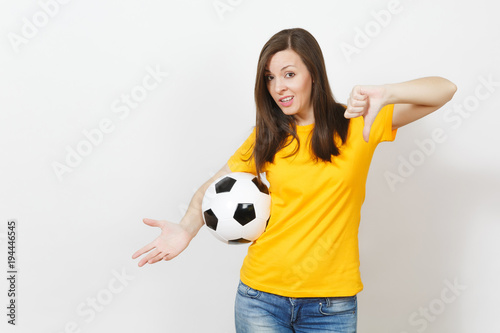 Pretty European young sad upset woman, football fan or player in yellow uniform holding soccer ball, showing thumb down isolated on white background. Sport, play football, healthy lifestyle concept. © ViDi Studio
