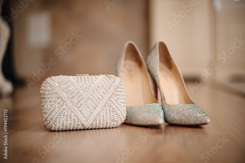 shoes of the bride with shiny pebbles stand next to a white clutch