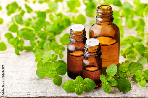 Oregano essential oil in the amber glass bottle and fresh oregano leaves