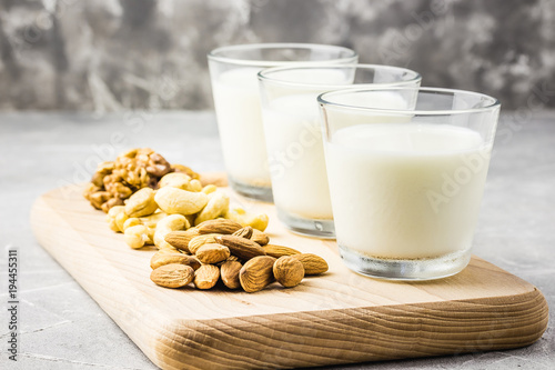Nut mix, almonds, cashew, walnuts and nut milk in glasses on wooden board on concrete background. Selective focus, copy space. 