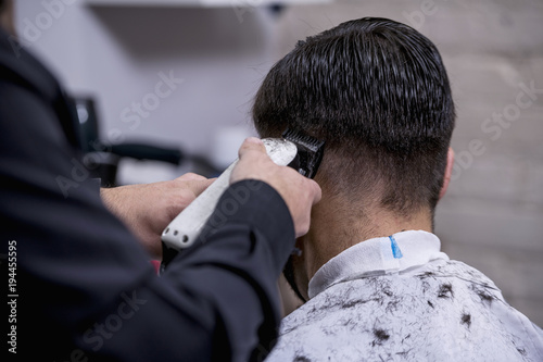 Hairdresser cutting hair to a client with an electric machine
