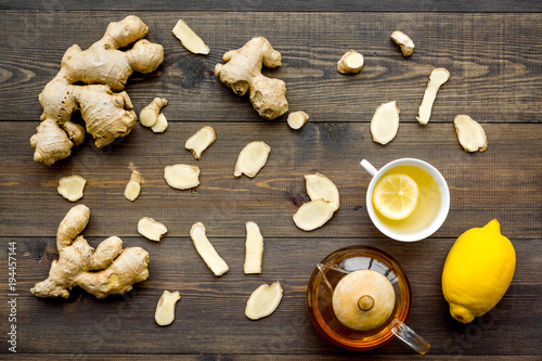 Tea for cure colds. Cup, teapot, ginger root and lemon on dark wooden background top view