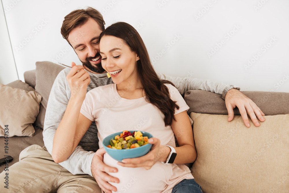 Cheerful young pregnant couple relaxing on a couch