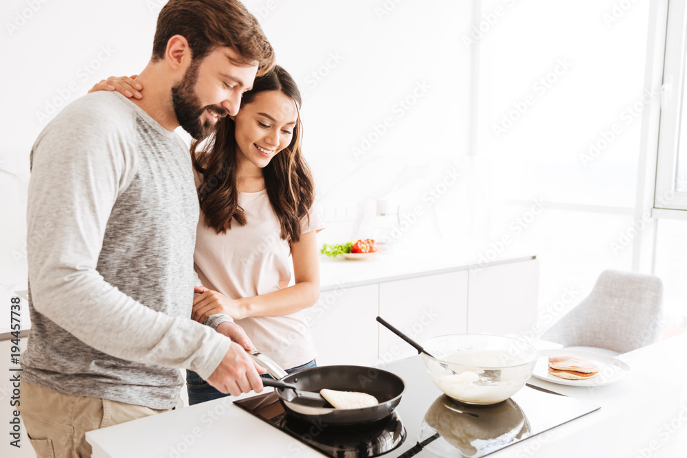 Portrait of a joyful young couple cooking pancakes Portrait of a joyful young couple cooking pancakes