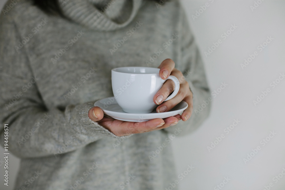 Breakfast and coffee theme: woman's hand holding white empty coffee or tea cup, advertising coffee or tea.