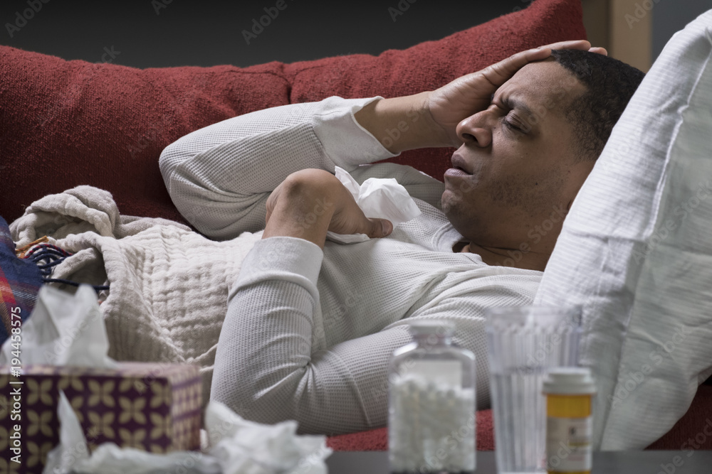 Foto Stock Man sick at home on a couch with tissues and pill bottles