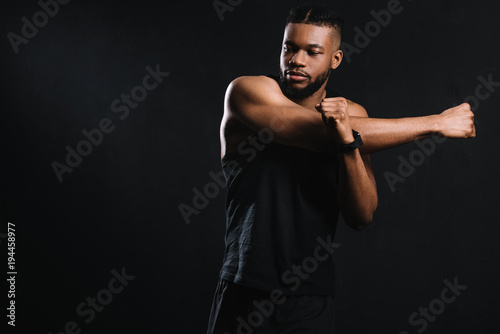 handsome athletic african american man stretching hands isolated on black © LIGHTFIELD STUDIOS