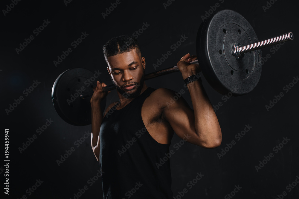 muscular young african american sportsman lifting barbell and looking at biceps on black muscular young african american sportsman lifting barbell and looking at biceps on black