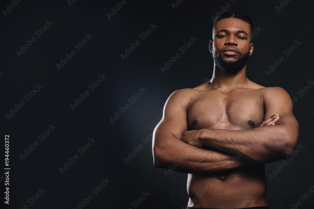 muscular shirtless young african american man standing with crossed arms and looking at camera isolated on black muscular shirtless young african american man standing with crossed arms and looking at camera isolated on black