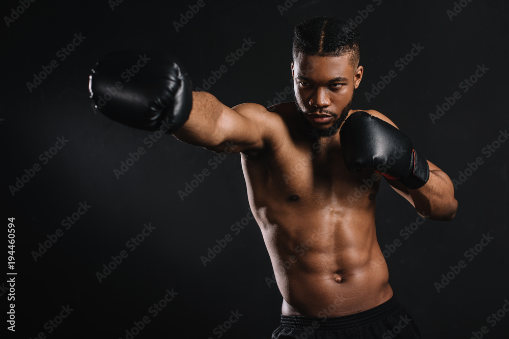young shirtless african american sportsman in boxing gloves training isolated on black