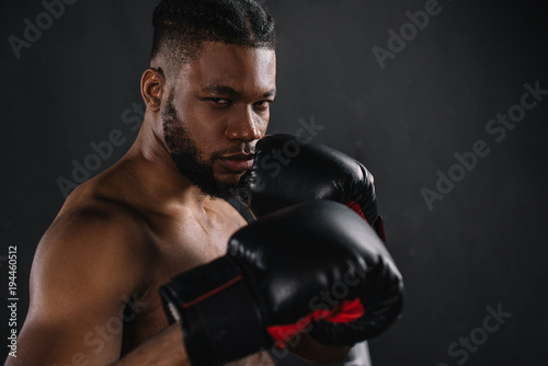 young shirtless african american boxer in boxing gloves looking at camera isolated on black © LIGHTFIELD STUDIOS