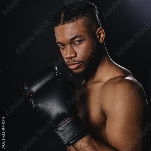 serious shirtless african american boxer in boxing gloves looking at camera isolated on black © LIGHTFIELD STUDIOS