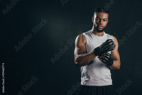 young african american kickboxer wearing gloves and looking at camera isolated on black